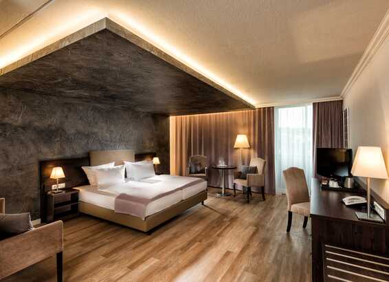 A modern deluxe hotel room features a large bed, ambient lighting, and elegant furnishings for a luxurious stay.