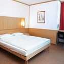 A cozy double room features a neatly made bed, a desk with a chair, and wall lighting, creating a welcoming atmosphere.