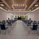 A spacious meeting room with rows of tables and chairs is set up for a conference, featuring a large screen at the front.