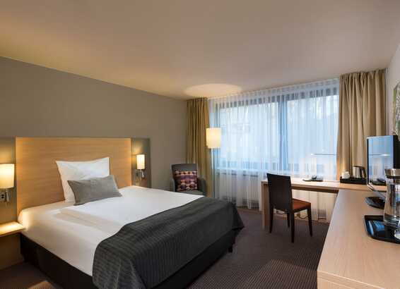 A cozy single room features a neatly made bed, a desk by the window, and modern decor, creating a comfortable standard setup.