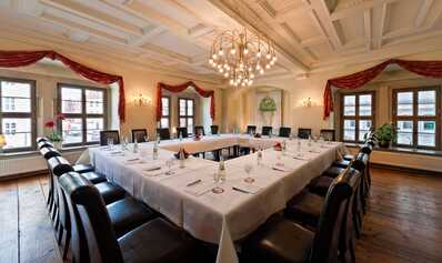 An elegant meeting room with a U-shaped table, set for a conference under a large chandelier.