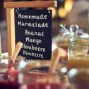 A breakfast spread features jars of homemade marmalade with a chalkboard listing flavors like mango and blueberry.