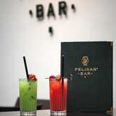 Two colorful cocktails, one green and one red, are elegantly presented on a table at Pelikan Bar.