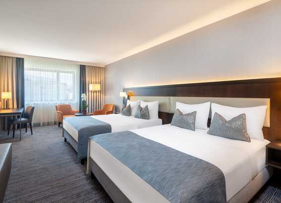 Ein modernes Hotelzimmer mit zwei Doppelbetten, einem Schreibtisch und einem großen Fenster sorgt für eine entspannte Atmosphäre.