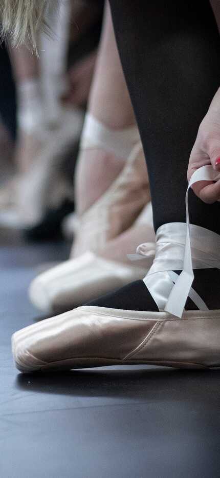 Tänzerinnen binden ihre Ballettschuhe, während sie sich auf eine Probe vorbereiten.