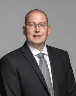 A man in a suit and tie poses confidently against a gray background.