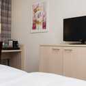 A modern hotel room features a cozy bed, desk with a coffee maker, abstract art, and a TV on a sleek cabinet.
