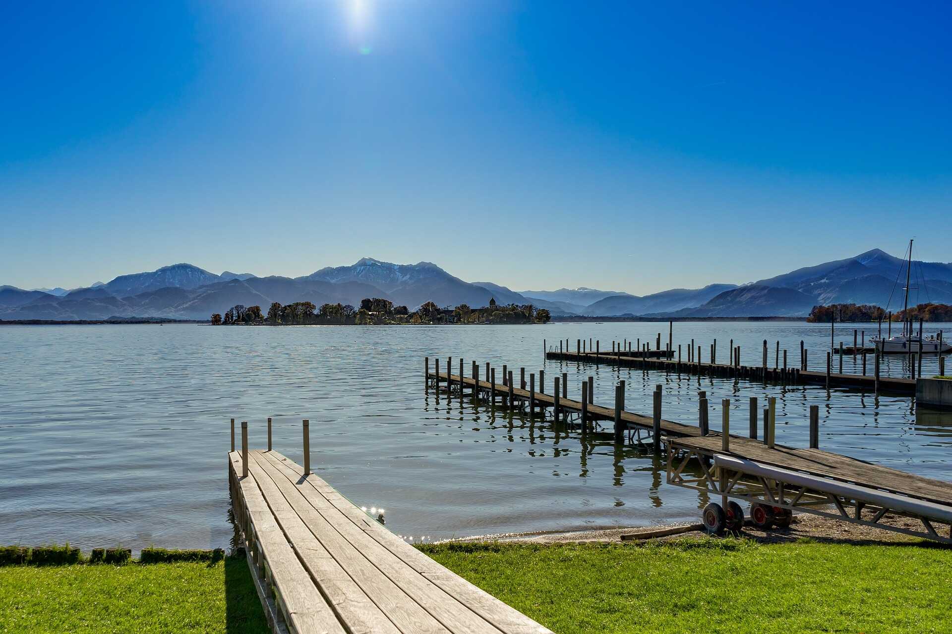 Wooden docks extend into a serene lake with majestic Alps in the background under a clear blue sky.