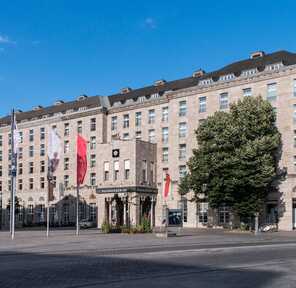 The Duisburg building exterior features classic architecture with flags and a tree under a clear blue sky.