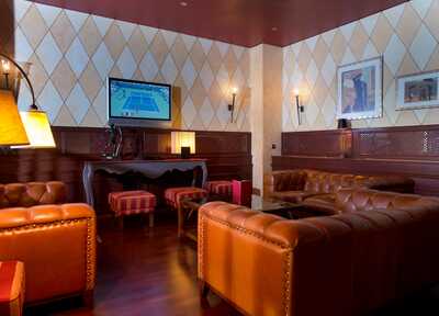 In einer eleganten Hotelbar mit Ledersofas läuft ein Tennis-Match auf einem Flachbildfernseher an der Wand.