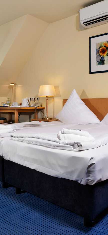A cozy double room features a neatly made bed, wicker chairs, and a table with wine, creating a welcoming atmosphere.