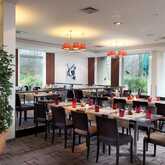 The modern restaurant features neatly arranged tables with red accents and large windows overlooking lush greenery.