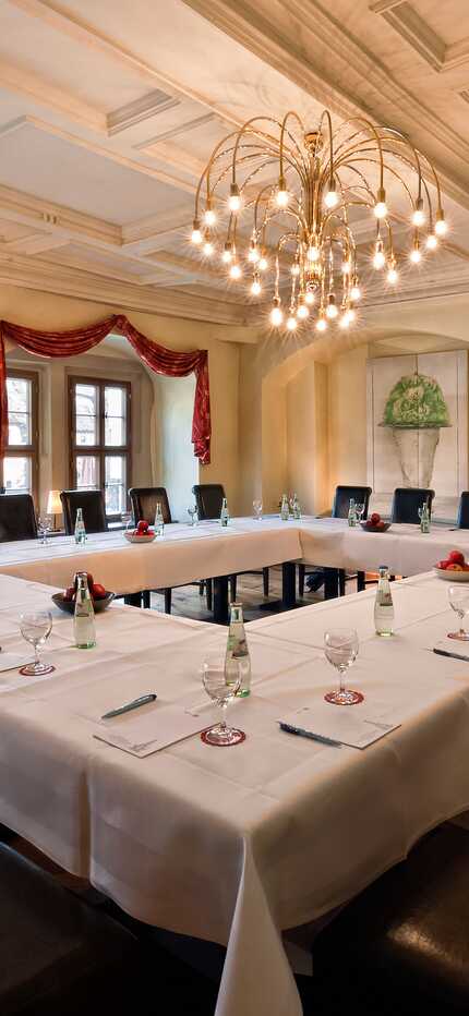 An elegant meeting room with a U-shaped table, set for a conference under a large chandelier.