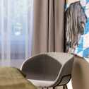 A cozy double room features a modern gray chair and a lion artwork on a blue and white patterned wall.