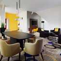 A modern living room features a black dining table, beige chairs, and bright yellow accents, creating a vibrant atmosphere.