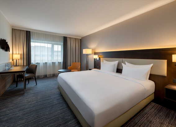 Modernes Hotelzimmer mit Doppelbett, Schreibtisch und gemütlichem Stuhl bei Tageslicht | © Name
