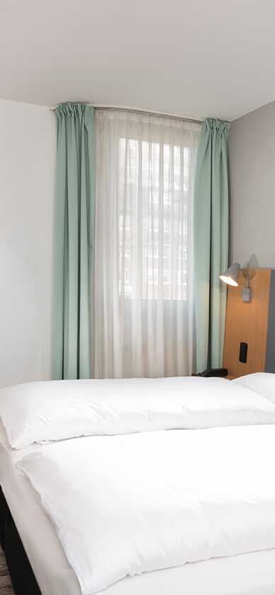 A modern double room features a neatly made bed, a desk with a chair, and an industrial artwork on the wall.