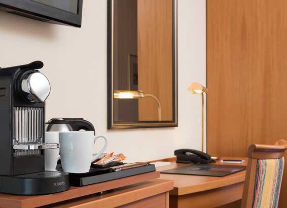 A cozy business room features a sleek coffee machine, a white mug, and a desk lamp, perfect for productive work sessions.