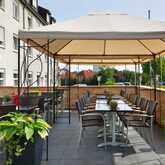 Eine Restaurantterrasse mit Sonnendach zeigt stilvoll gedeckte Tische und üppige Pflanzen in einer einladenden Atmosphäre.