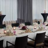A festively decorated dining room features elegantly set tables with candles, folded napkins, and floral centerpieces.