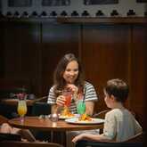Eine Frau genießt mit zwei Kindern bunte Cocktails und Essen in einem gemütlichen Restaurant.