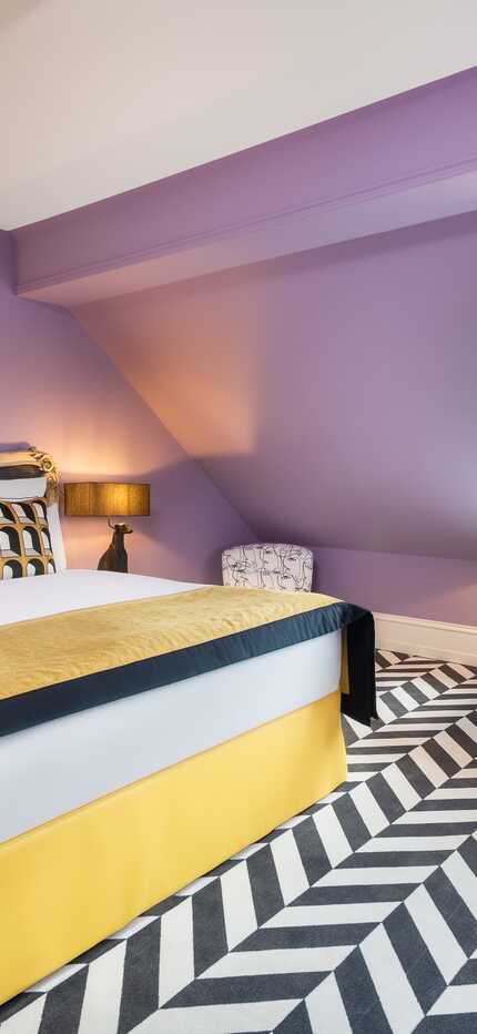 Ein stilvolles Boutique-Zimmer mit lila Wänden, einem eleganten Bett und einem großen Fenster mit Blick ins Grüne.