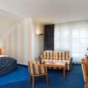 A bright business hotel room features a cozy bed, striped sofa, and a small desk, ideal for work and relaxation.
