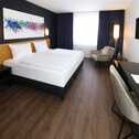 A modern hotel room features a large bed, abstract wall art, and a sleek desk, creating a superior relaxation space.