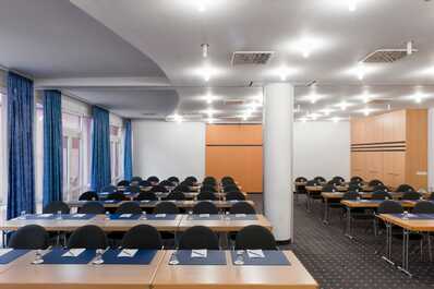 A modern conference room is set up with rows of tables and chairs, ready for a meeting.