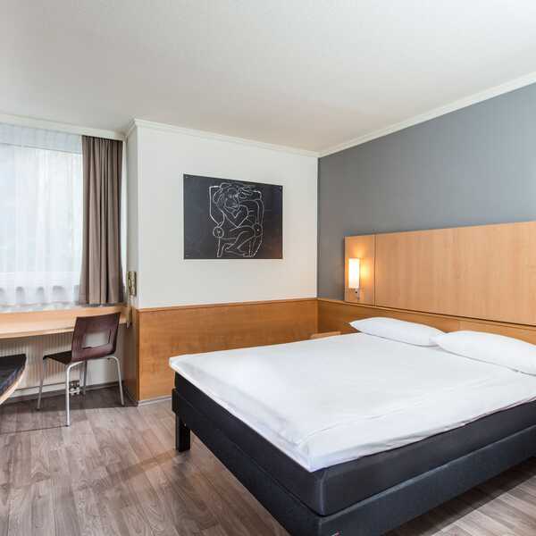 Ein modernes Einzelzimmer mit einem gemütlichen Bett, Schreibtisch und stilvoller Kunst an der Wand.