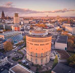 Aerial view of the historic Wasserturm hotel amidst the vibrant cityscape at sunset.