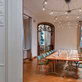 A well-lit meeting room features a long table with water bottles and paper, surrounded by green chairs under elegant lighting.