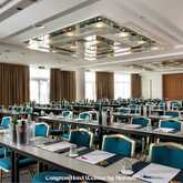 A spacious conference room with neatly arranged tables and chairs, set up for a meeting with papers and water bottles.