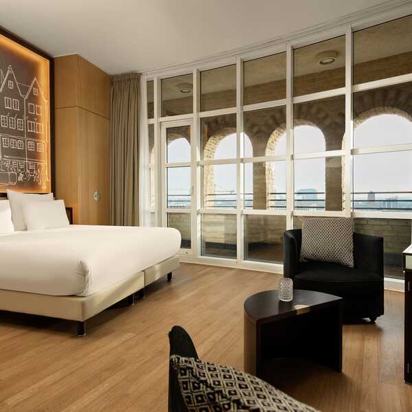 Ein modernes Schlafzimmer mit großem Fenster bietet Blick auf einen Wasserturm und ist stilvoll eingerichtet mit Kunstwerk.