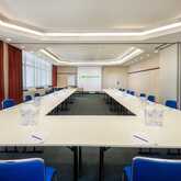 A spacious conference room features a U-shaped table setup with blue chairs and a projection screen displaying a logo.
