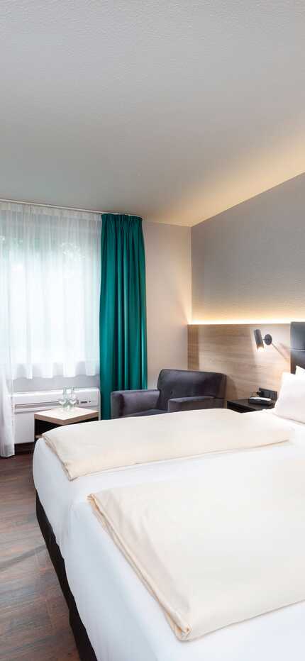 Ein modernes und komfortables Doppelzimmer im Best Western Hotel Achim Bremen. Es verfügt über zwei Einzelbetten mit dunklem Kopfteil und weißer Bettwäsche. Links vom Bett befindet sich ein Schreibtisch mit Stuhl und einem Fernseher an der Wand. Der Raum