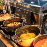 An inviting breakfast buffet features sausages, eggs, and beans, with a focus on hearty options like rösti and bacon.