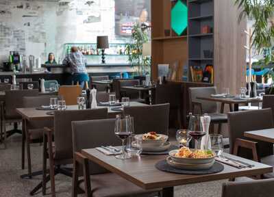 Ein stilvolles Restaurant mit gedeckten Tischen und zwei Personen an der Bar im Hintergrund.