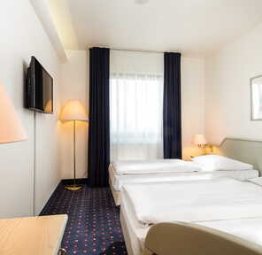 Ein helles Zweibettzimmer mit zwei Einzelbetten, einem Fernseher und gemütlicher Beleuchtung lädt zum Entspannen ein.