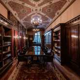A luxurious library features ornate wooden shelves, elegant chandeliers, and a long table for reading or meetings.
