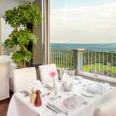 Ein elegant gedeckter Tisch in einer Sky-Bar mit Panoramablick auf eine grüne Landschaft durch große Fenster.