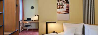 A modern business room features a cozy bed, a work desk with a laptop, and a stylish decor on the wall.
