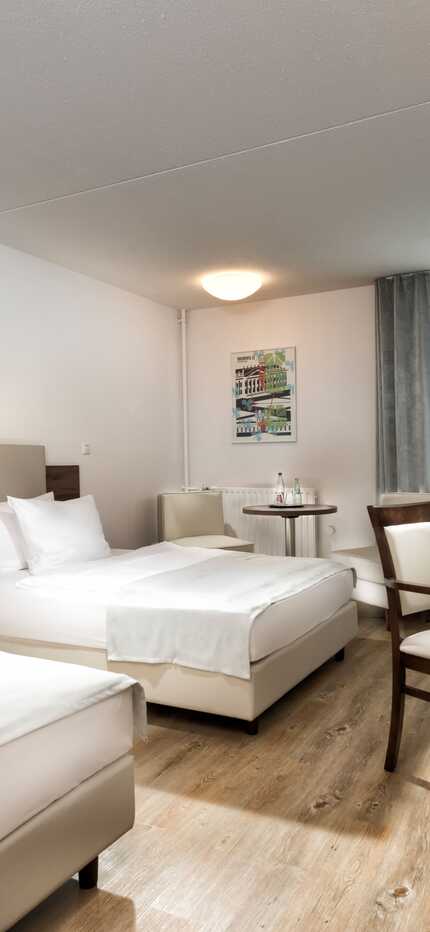 A modern business hotel room with twin beds, a desk, and a TV, featuring minimalist decor and natural light through a window.