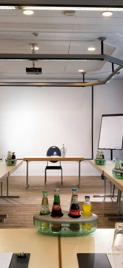 A well-lit meeting room in Hessen is set up with tables, chairs, beverages, and presentation tools for a conference.