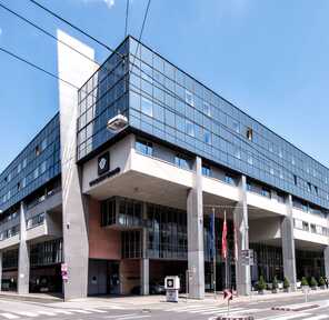 A modern glass-fronted building stands prominently on a sunny day, showcasing its sleek exterior design.