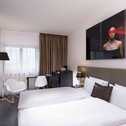 A modern double room features a large bed, stylish decor, and an eye-catching art piece above the headboard.