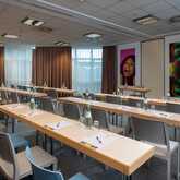 A conference room with neatly arranged tables and chairs is ready for a meeting, featuring colorful portraits on the wall.