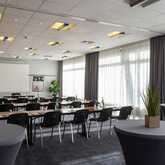 A well-lit conference room is set up with tables, chairs, and plants, ready for a meeting or seminar.