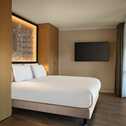 Modern bedroom with a large bed, wooden accents, and a wall-mounted TV, featuring a lit cityscape artwork.