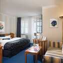 A cozy hotel room features a double bed, a striped sofa, and a coffee machine, creating a comfortable business environment.
